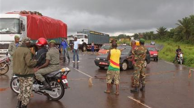 In this photo taken on Tuesday, Aug. 12,  2014,  Guinea soldiers stand around a  rope across the road that separates Guinea and Sierra Leone, and works as a makeshift border control checkpoint at  Gbalamuya-Pamelap, Guinea. As Guinea closed its border with Sierra Leone at the weekend in an attempt to halt the spread of the deadly Ebola virus, people and goods were not able to cross to either side.  (AP Photo/ Youssouf Bah)