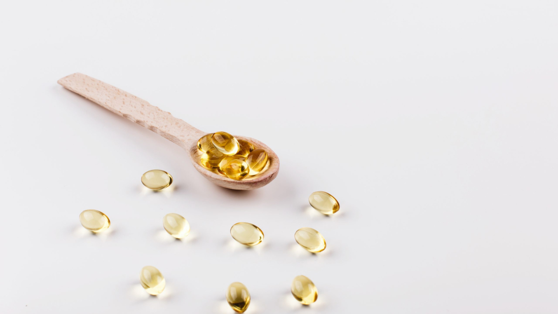 Oil capsule for hair with vitamin E lie on wooden spoon