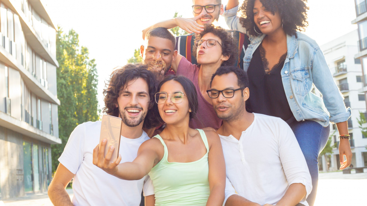 Joyous mix raced people taking group selfie outdoors. Interracial team of friends posing, grimacing, gesturing and smiling at phone camera. Photo concept