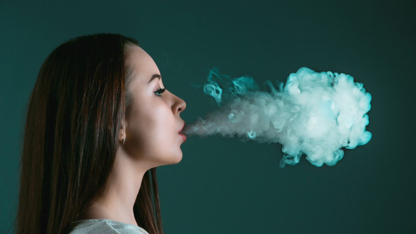 The face of vaping young woman on black studio background