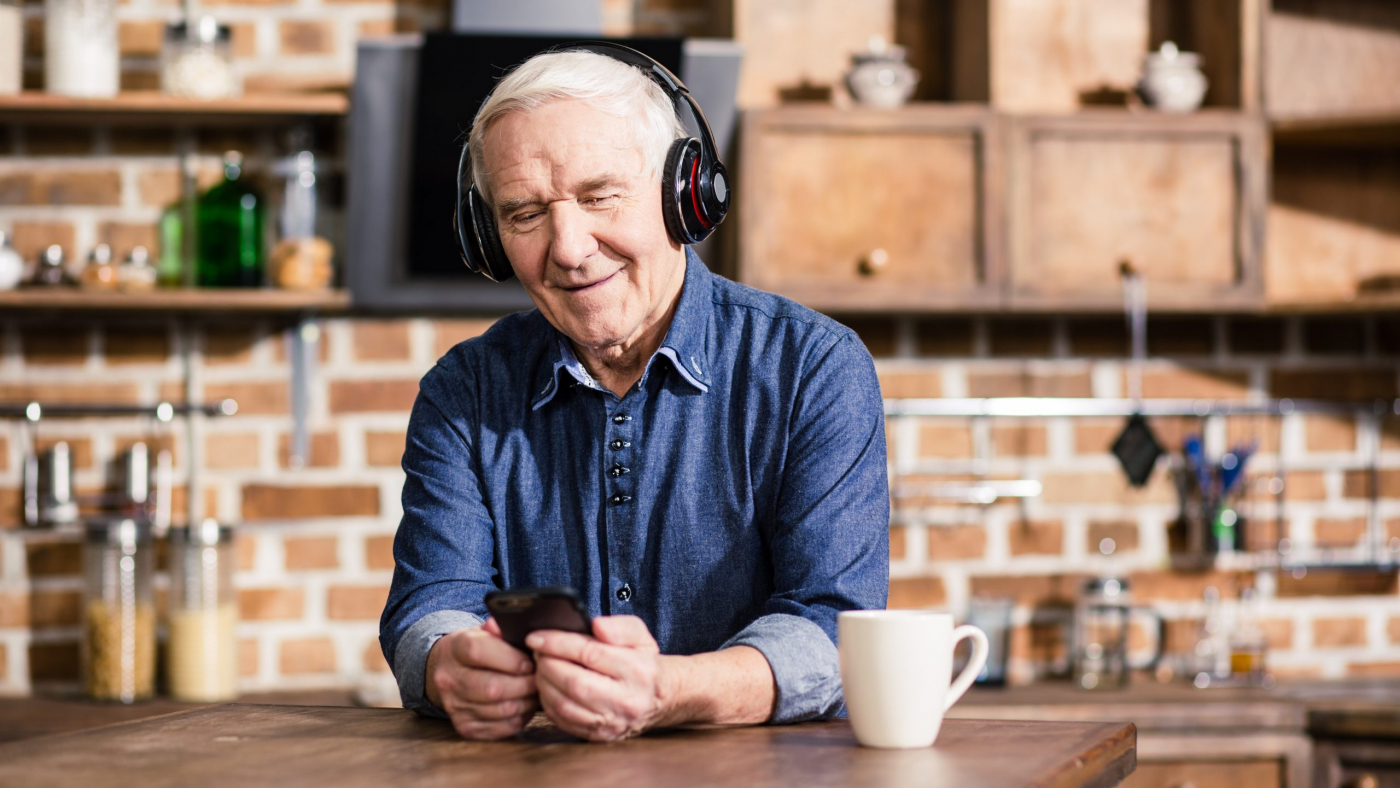 Switch it on. Pleasant smiling elderly man using his smartphone while listening to music