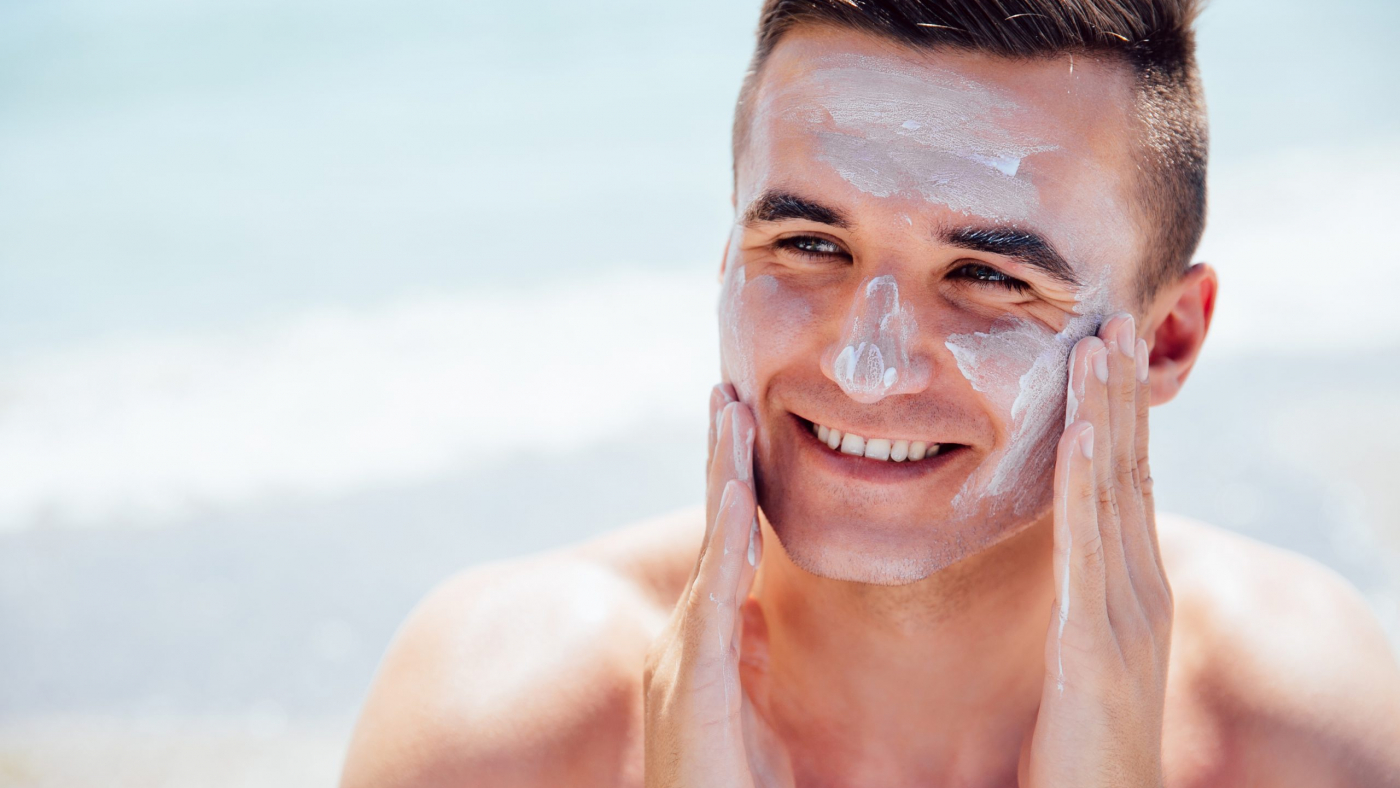 Smiling man putting tanning cream on his face, takes a sunbath on the beach. Healthcare.