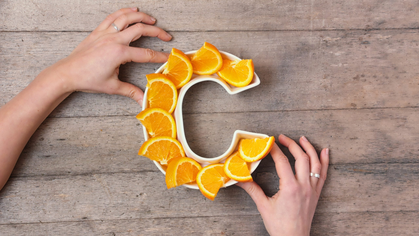 Vitamin C nutrient in food concept. Woman hands holding plate in shape of letter C with orange slices on wooden background. Flat lay or top view. Ascorbic acid is important for immune system function.