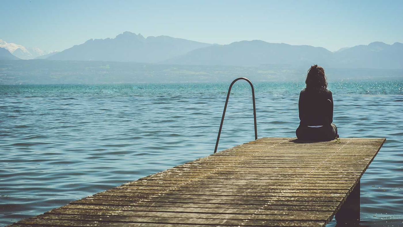 Youg Girl Experiencing Depression Site on Pier Looking Over Lake