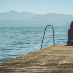 Youg Girl Experiencing Depression Site on Pier Looking Over Lake